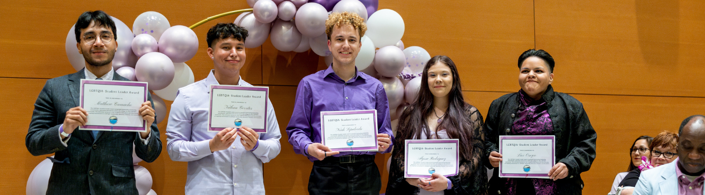 Five students stand holding paper awards.